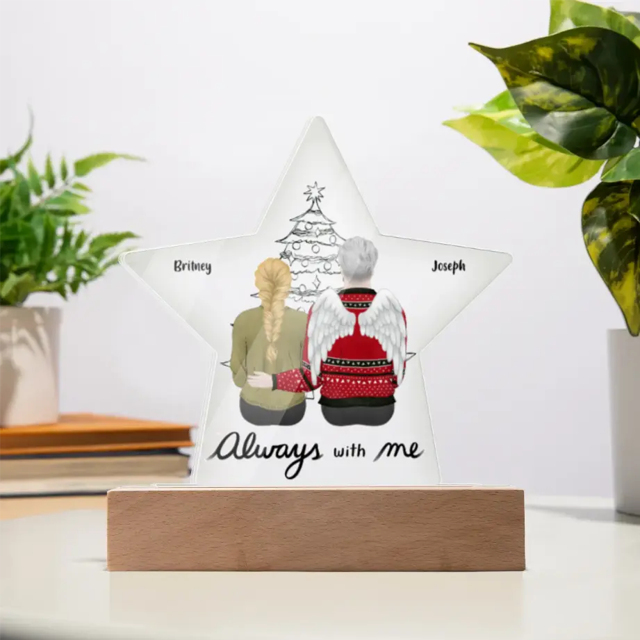 Personalized acrylic star plaque with angel and woman illustration, names Britney and Joseph, Christmas tree background, and 'Always with me' message on wooden base.